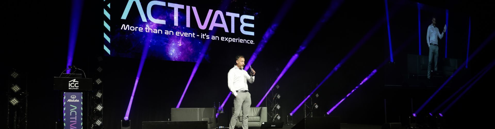 Man standing on stage against purple gradient screen for All State conference