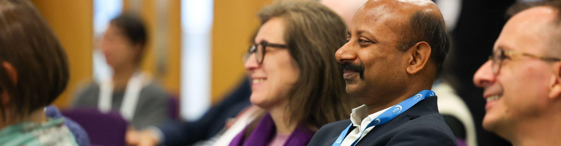 Close up image of two men and one woman smile in an audience of people at a conference